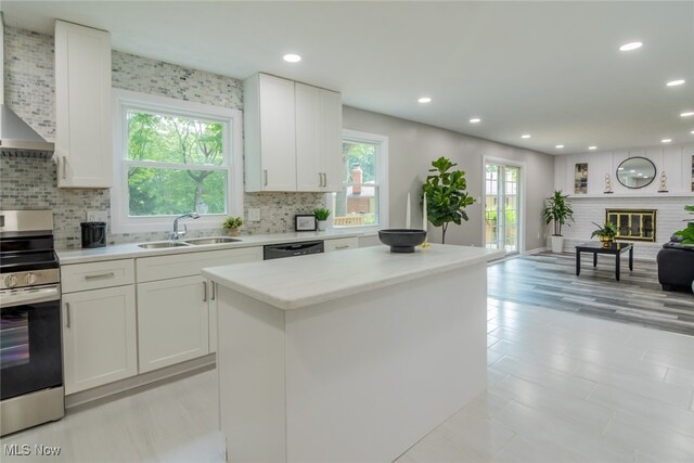 kitchen with sink, white cabinetry, wall chimney exhaust hood, and stove