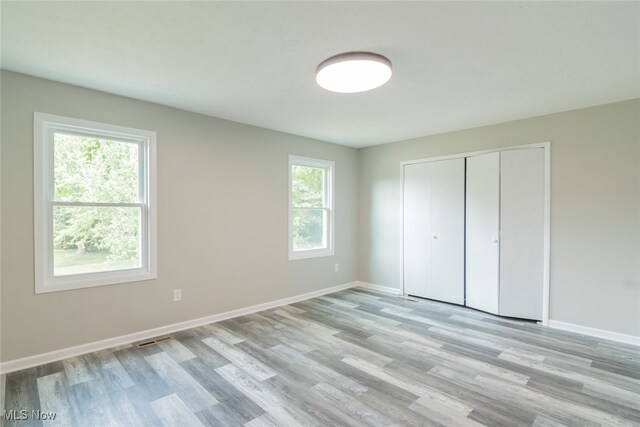 unfurnished bedroom with multiple windows, a closet, and light hardwood / wood-style flooring