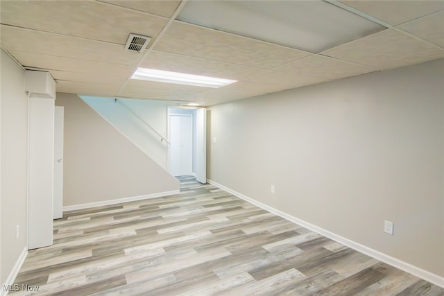 basement featuring a paneled ceiling and light hardwood / wood-style flooring