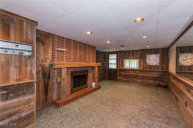 interior space featuring light colored carpet, a fireplace, wood walls, and a paneled ceiling