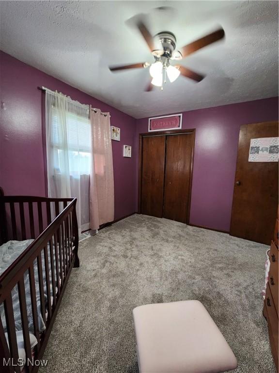 bedroom with light carpet, a textured ceiling, a closet, a nursery area, and ceiling fan