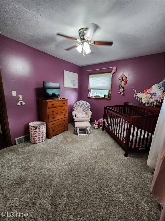 carpeted bedroom with ceiling fan, a nursery area, and a textured ceiling