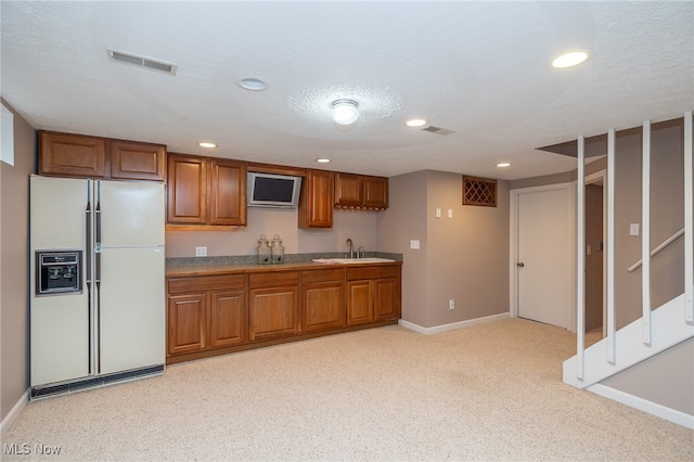 kitchen featuring white refrigerator with ice dispenser, sink, and a textured ceiling