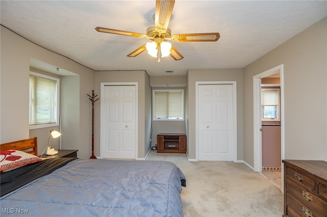 carpeted bedroom with multiple windows, ceiling fan, a textured ceiling, and two closets