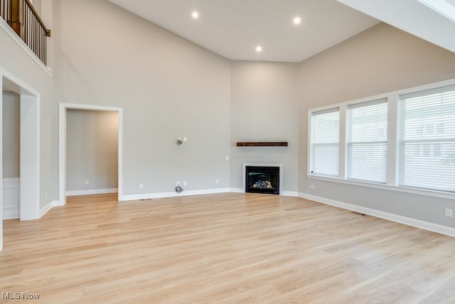 unfurnished living room with light wood-type flooring and high vaulted ceiling