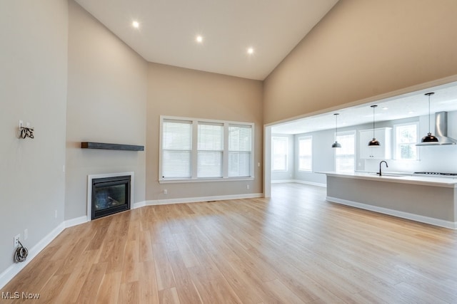 unfurnished living room with light wood-type flooring, plenty of natural light, and high vaulted ceiling