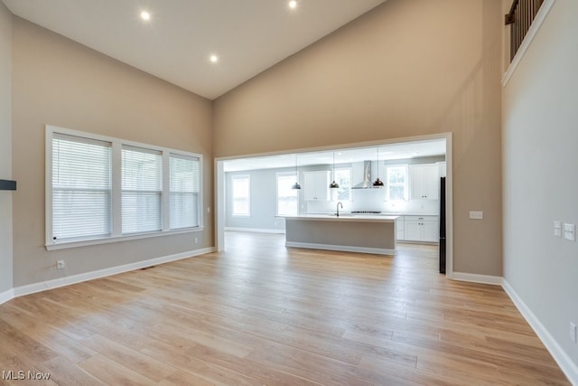 unfurnished living room with high vaulted ceiling, sink, and light hardwood / wood-style flooring