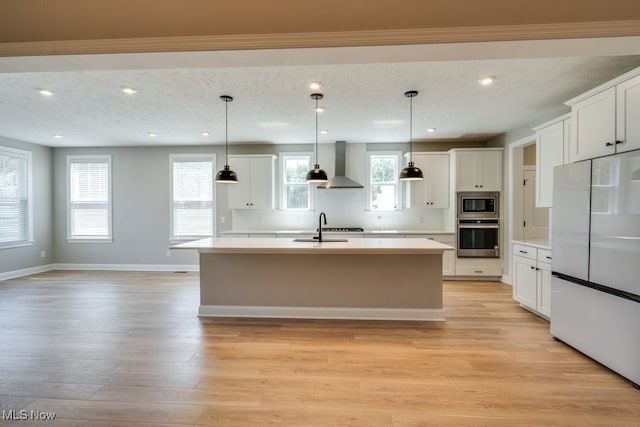 kitchen featuring a kitchen island with sink, appliances with stainless steel finishes, wall chimney exhaust hood, and light hardwood / wood-style flooring