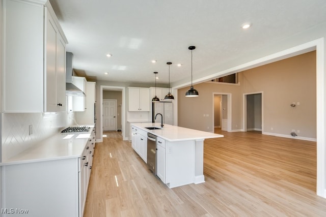 kitchen featuring backsplash, light hardwood / wood-style floors, an island with sink, wall chimney range hood, and white cabinets