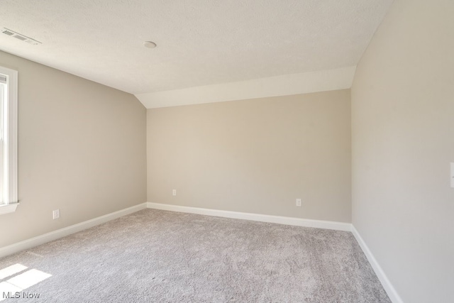 carpeted spare room with a textured ceiling and vaulted ceiling