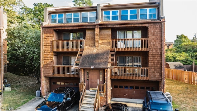 rear view of property with a balcony, central AC, and a garage