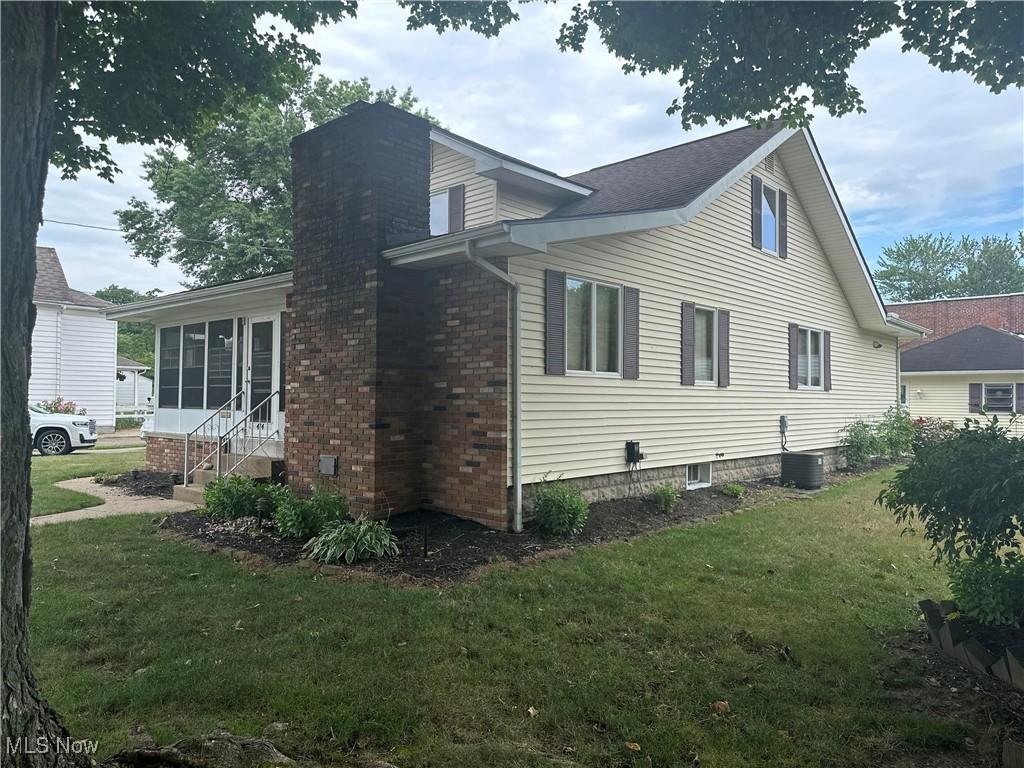 view of side of home featuring a sunroom, central air condition unit, a chimney, and a yard