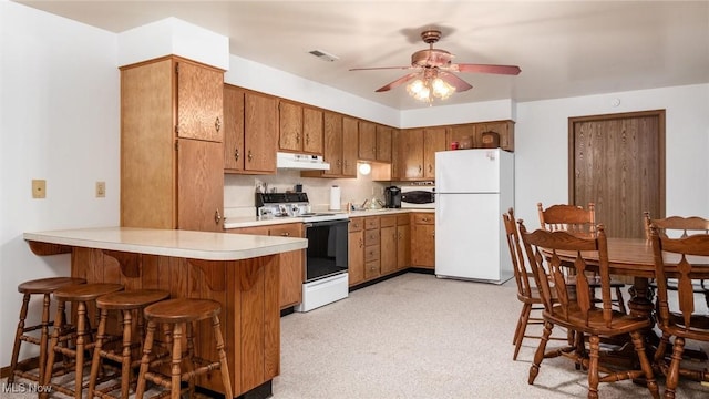 kitchen with visible vents, brown cabinets, under cabinet range hood, white appliances, and a peninsula