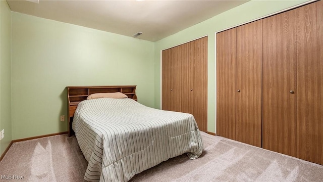 carpeted bedroom with visible vents, multiple closets, and baseboards