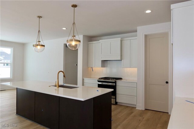 kitchen with sink, white cabinets, gas range, and a center island with sink