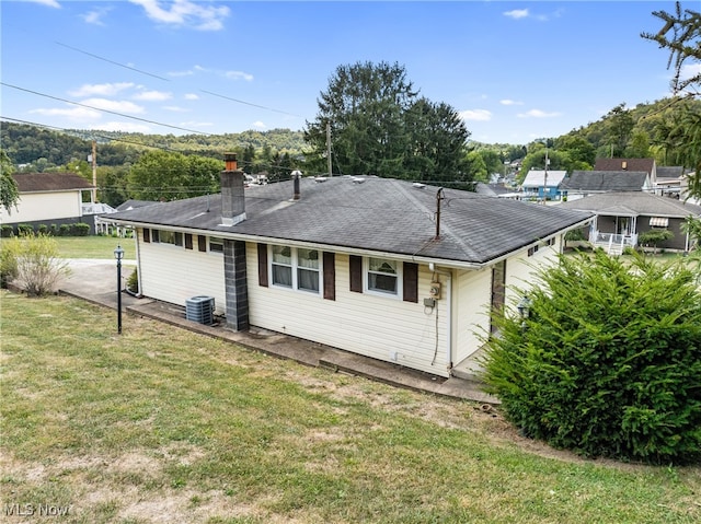 rear view of house featuring central AC unit and a lawn