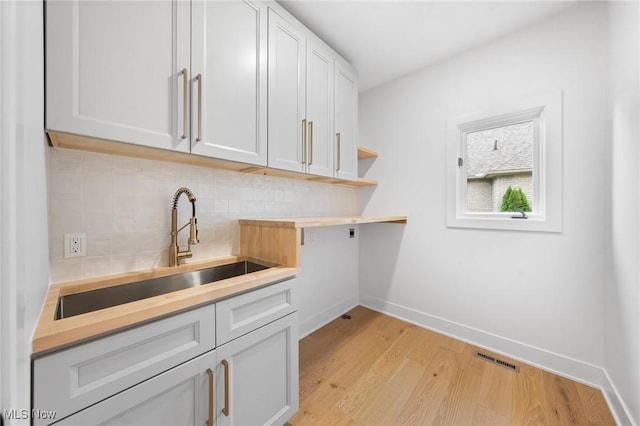 washroom featuring visible vents, baseboards, light wood-style flooring, cabinet space, and a sink