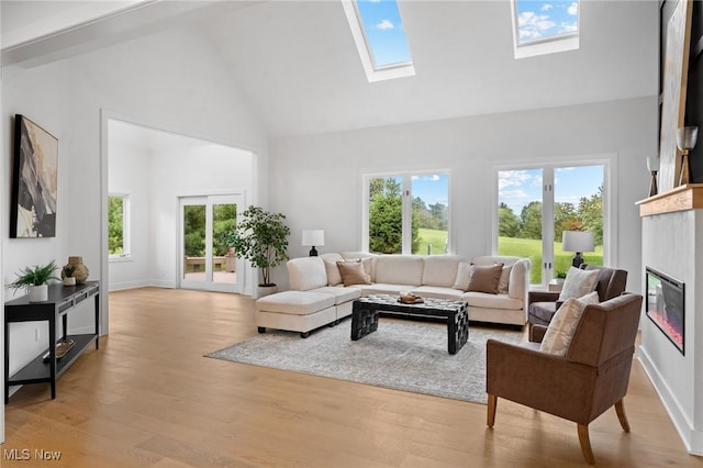 living room with baseboards, light wood-style flooring, a skylight, a glass covered fireplace, and high vaulted ceiling