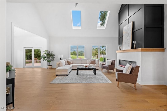 living area with a glass covered fireplace, high vaulted ceiling, and light wood-type flooring