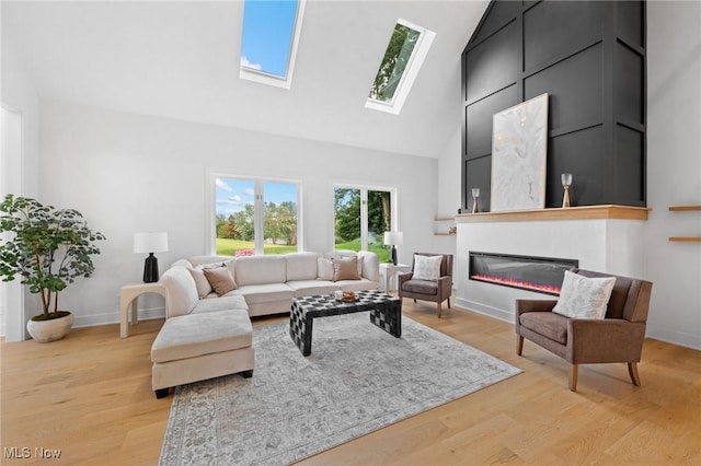 living area with light wood finished floors, a glass covered fireplace, a high ceiling, and baseboards