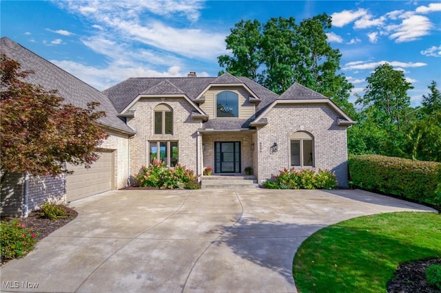 french country style house featuring concrete driveway, a shingled roof, a garage, brick siding, and a chimney