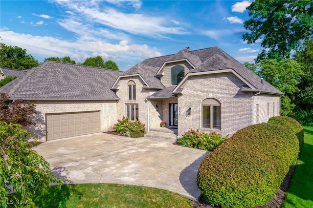 french country inspired facade featuring brick siding, concrete driveway, a garage, and roof with shingles