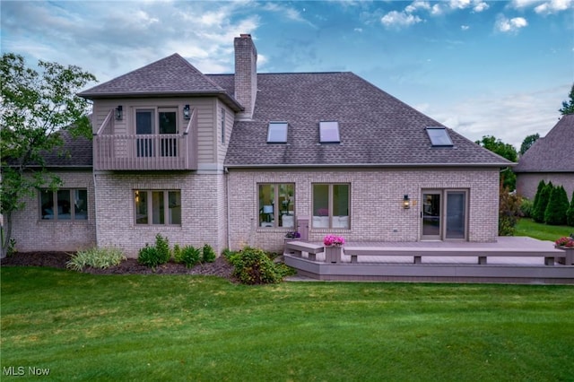 rear view of property featuring roof with shingles, a yard, a chimney, a deck, and brick siding