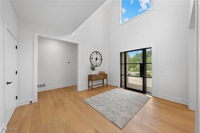 foyer featuring visible vents, baseboards, a high ceiling, and light wood-style flooring