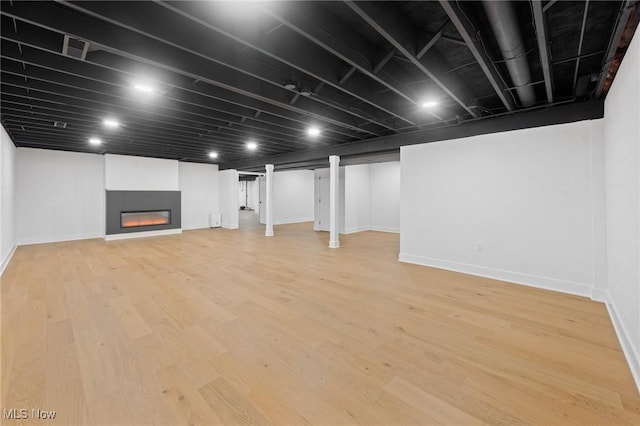 finished basement with a glass covered fireplace, light wood-style flooring, and baseboards