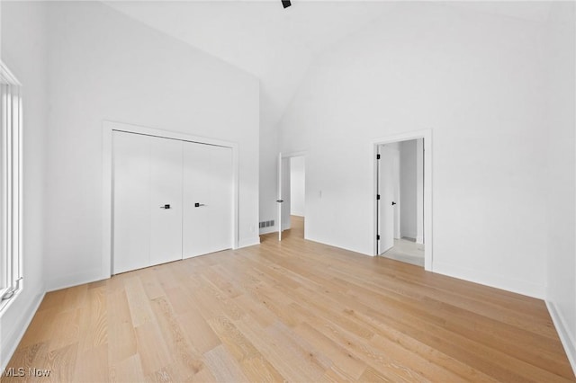 unfurnished bedroom with visible vents, a high ceiling, light wood-style floors, and a closet