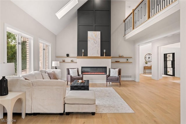 living room featuring visible vents, light wood finished floors, a skylight, a towering ceiling, and a glass covered fireplace