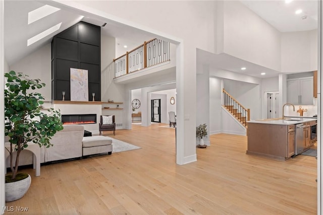 living area featuring stairway, baseboards, light wood-style flooring, a high ceiling, and a fireplace