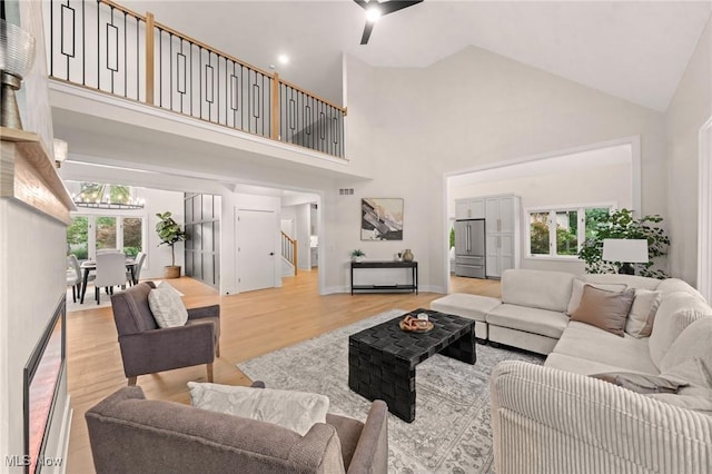 living room featuring visible vents, light wood finished floors, high vaulted ceiling, an inviting chandelier, and stairs