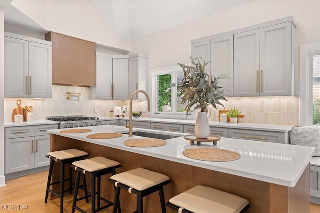 kitchen with a sink, light wood finished floors, decorative backsplash, light countertops, and vaulted ceiling