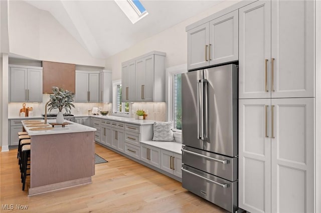 kitchen featuring light wood finished floors, lofted ceiling with skylight, gray cabinetry, and freestanding refrigerator