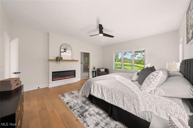 bedroom with a glass covered fireplace, a ceiling fan, baseboards, and wood finished floors