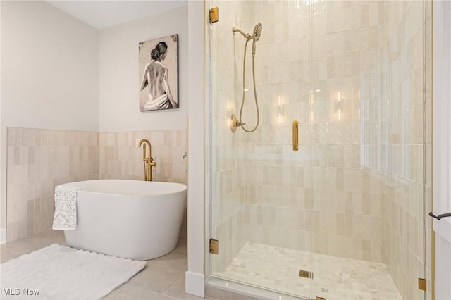 bathroom featuring tile patterned flooring, a stall shower, a freestanding bath, and tile walls