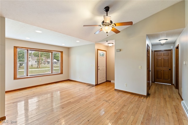 empty room featuring light wood-type flooring, a baseboard heating unit, vaulted ceiling, and ceiling fan