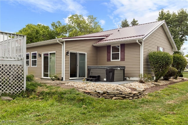 rear view of property featuring a lawn and a hot tub