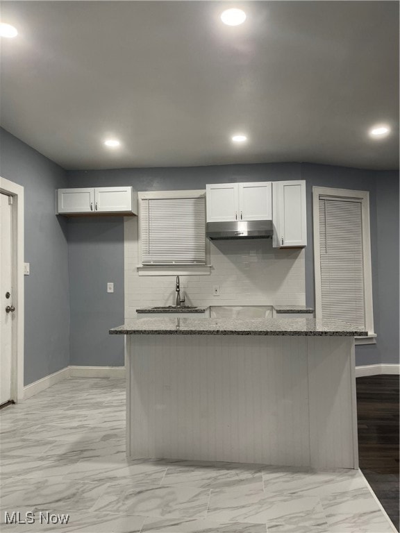 kitchen with light wood-type flooring, backsplash, white cabinets, sink, and stone counters