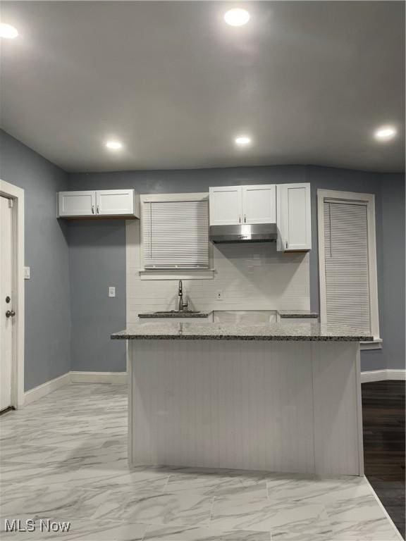 kitchen featuring backsplash, a center island, under cabinet range hood, dark stone counters, and a sink