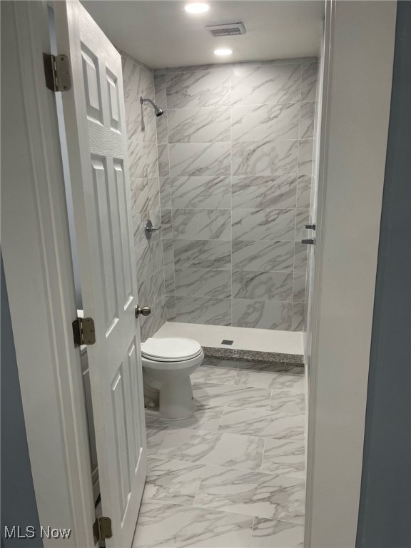 bathroom featuring tile patterned flooring, a tile shower, and toilet