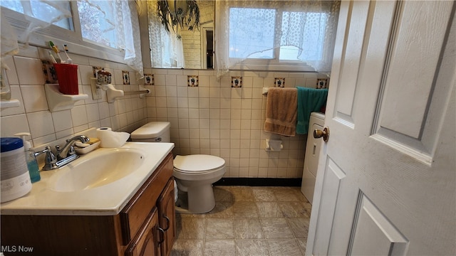 bathroom with a wealth of natural light, toilet, vanity, and tile walls