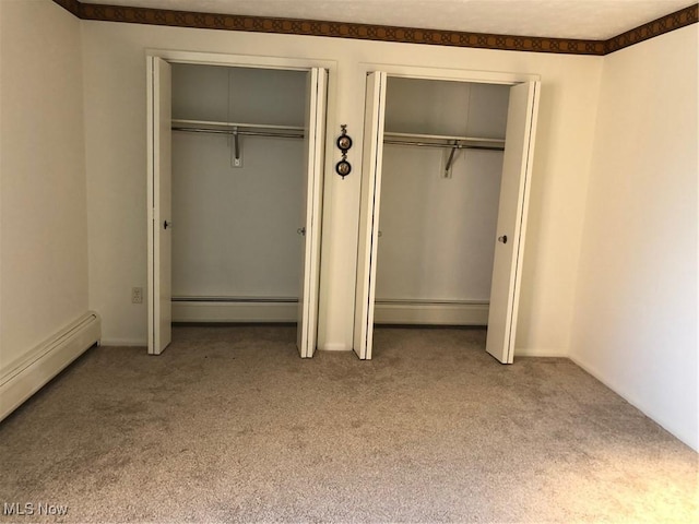 unfurnished bedroom with baseboards, carpet flooring, a baseboard heating unit, and two closets
