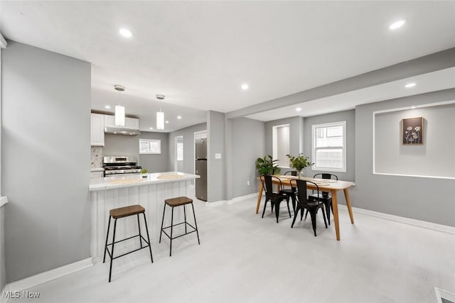 kitchen with stainless steel appliances, a kitchen breakfast bar, light stone counters, decorative light fixtures, and white cabinets