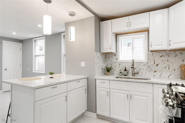 kitchen featuring gas range, sink, light stone counters, decorative light fixtures, and white cabinets