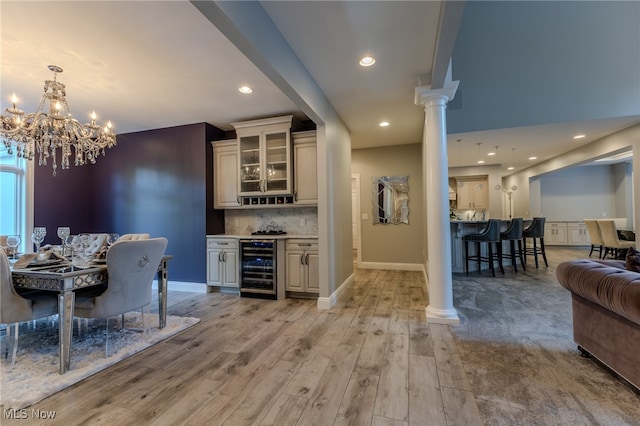 bar with pendant lighting, tasteful backsplash, beverage cooler, decorative columns, and light hardwood / wood-style floors