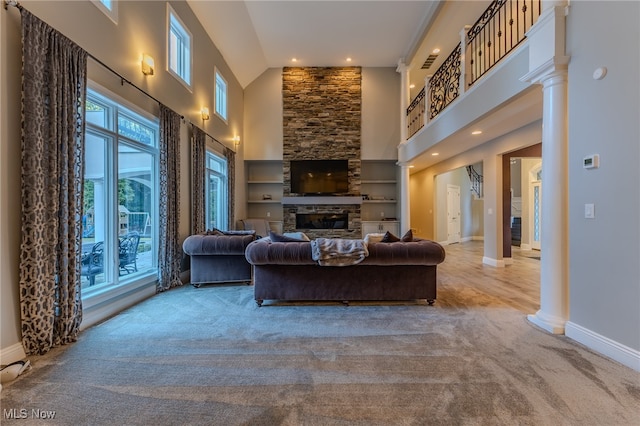 living room with decorative columns, a stone fireplace, carpet, and high vaulted ceiling