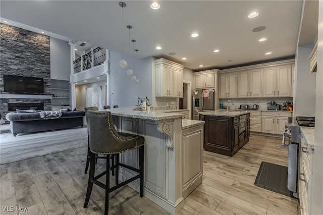 kitchen featuring light stone counters, decorative light fixtures, a fireplace, a breakfast bar area, and light wood-type flooring