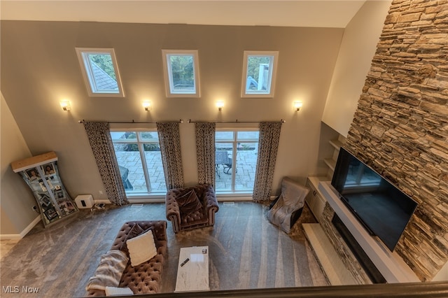 carpeted living room with a stone fireplace and a high ceiling